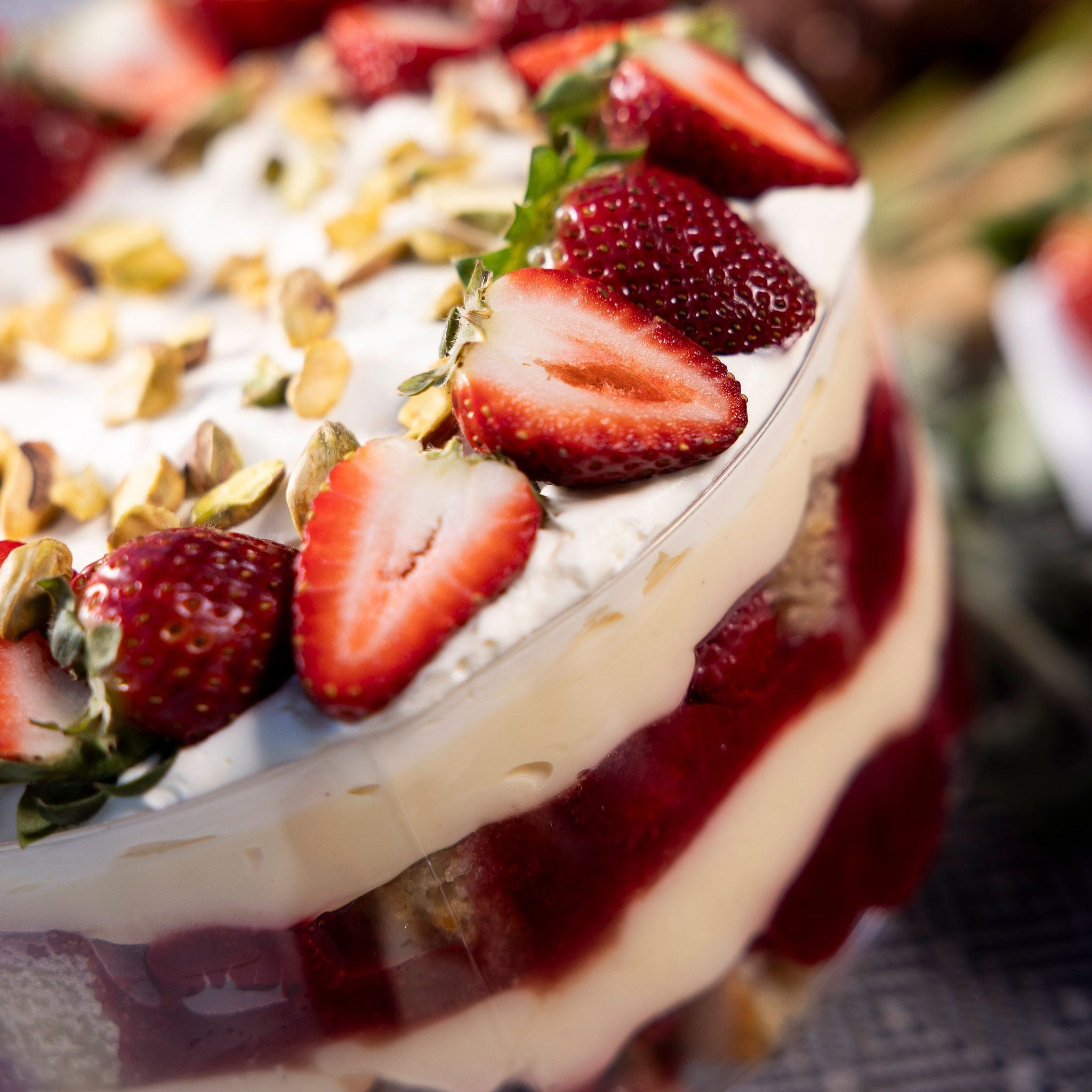 A bowl of trifle, topped with cream, strawberries & pistachios