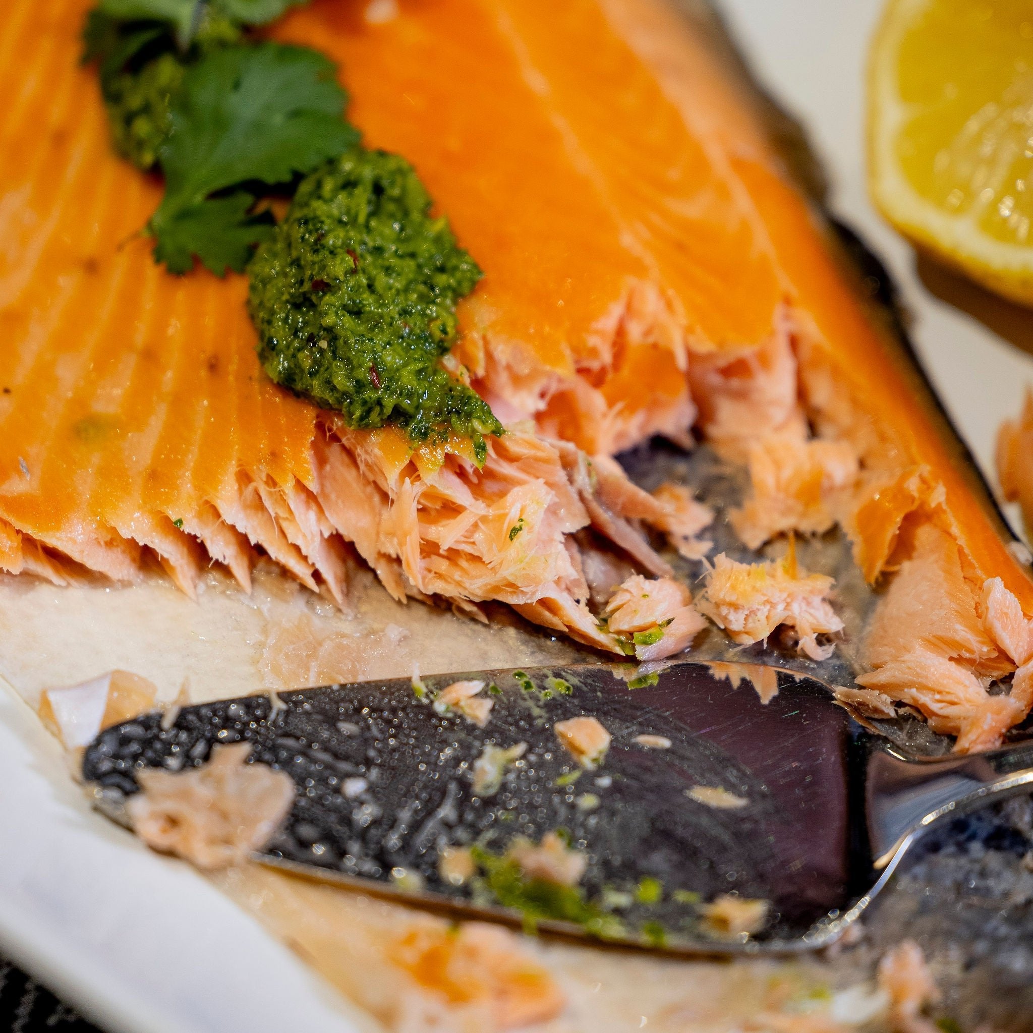 A side of salmon sits on a white platter.  It has been partially served and there is a cake slide on the platter.