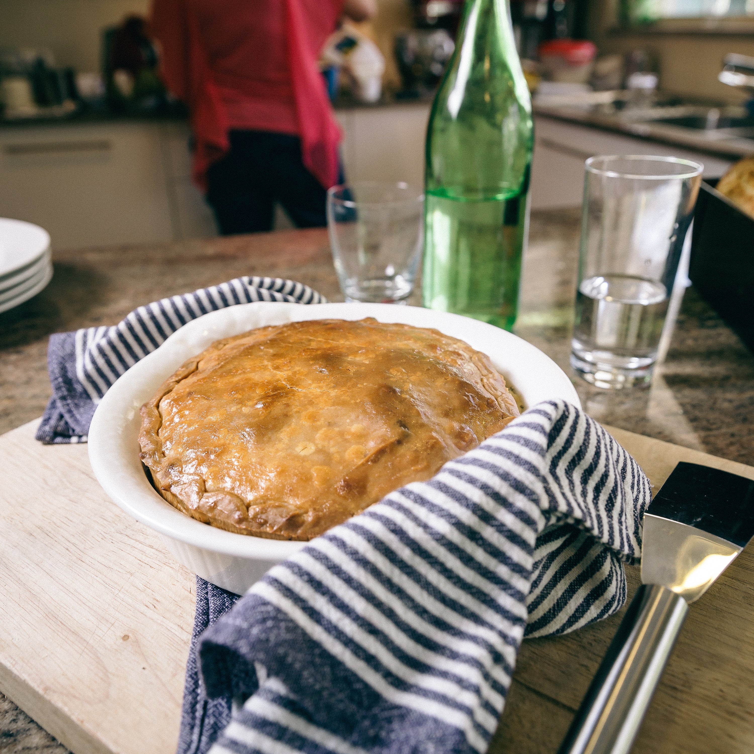 A homemade pie sitting on a kitchen bench with someone standing in the background.